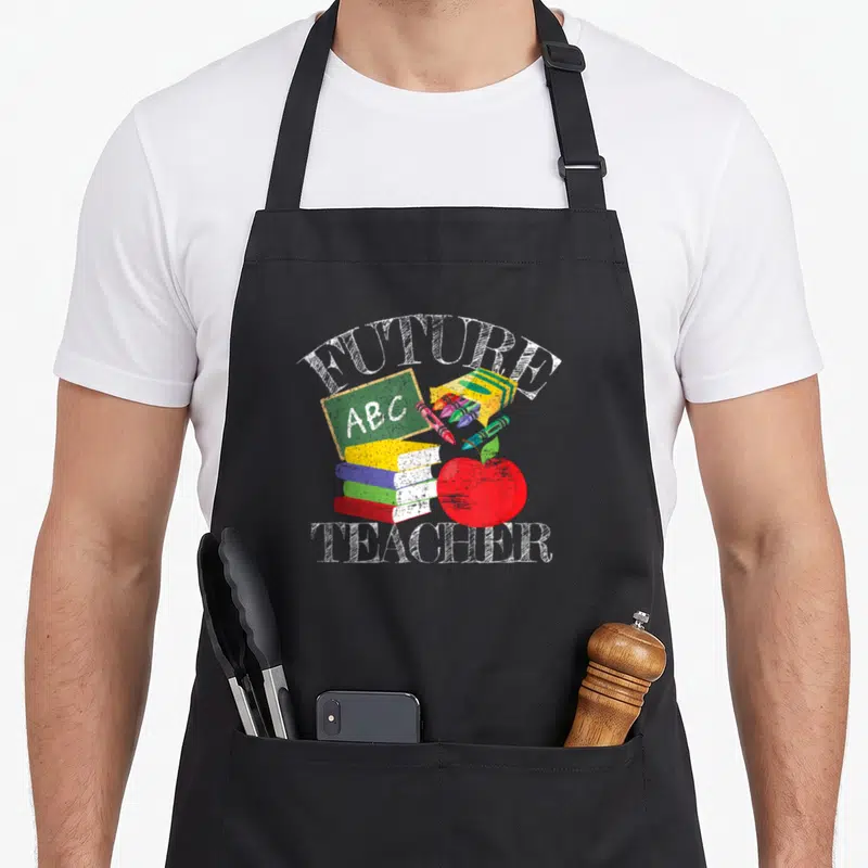 Costume teacher apron - FUTURE TEACHER text with books, ABC chalkboard, crayons, and red apple in cartoon style — shown on a black cotton canvas apron against a white background
