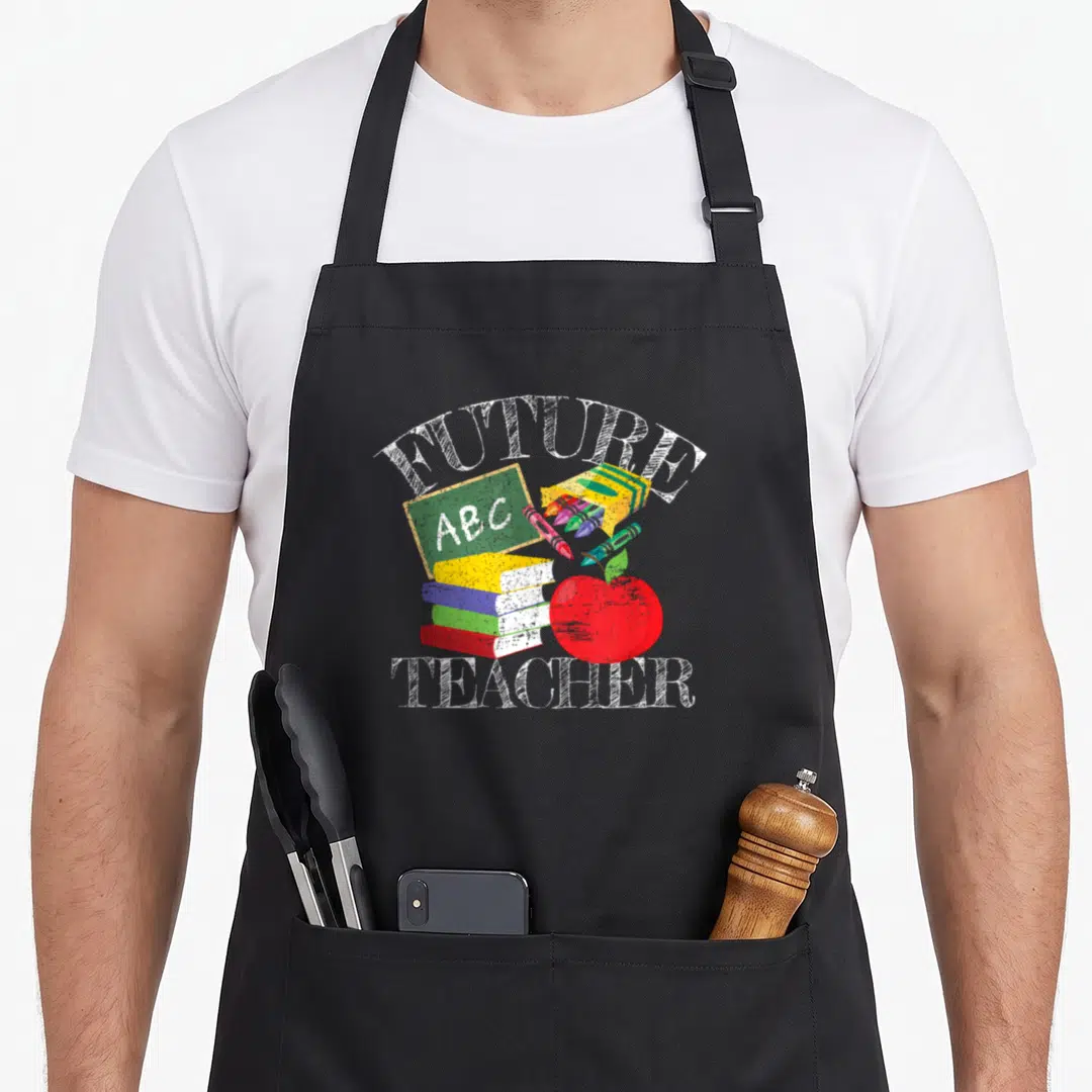 Costume teacher apron - FUTURE TEACHER text with books, ABC chalkboard, crayons, and red apple in cartoon style — shown on a black cotton canvas apron against a white background