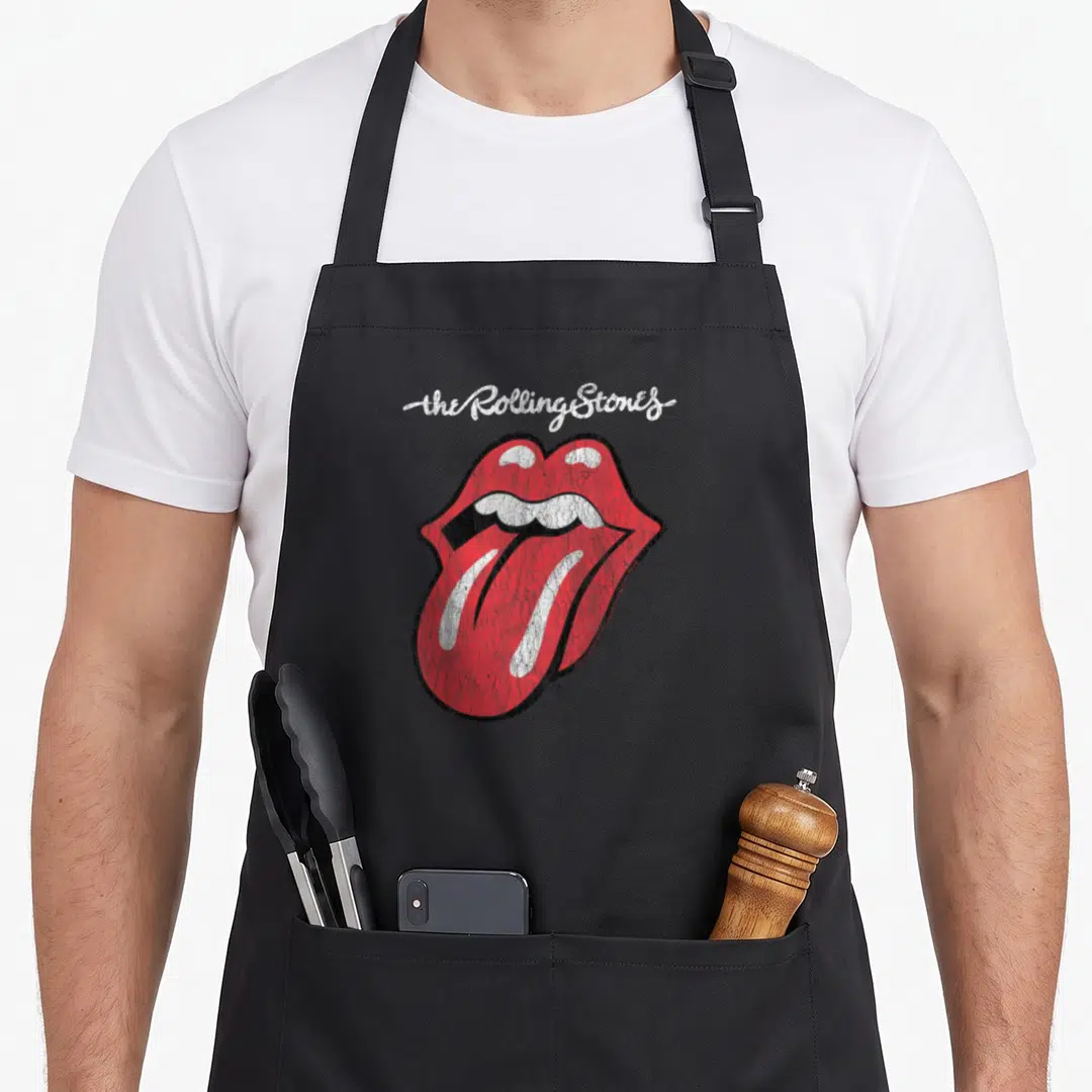 Script tongue rolling stones apron - Arched white script above red open lips with protruding tongue in retro style — shown on a black cotton canvas apron against a white background
