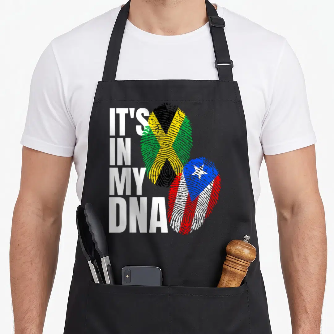 Jamaican heritage aprons - IT'S IN MY DNA text next to fingerprint flags of Jamaica and Puerto Rico — shown on a black cotton canvas apron against a white background