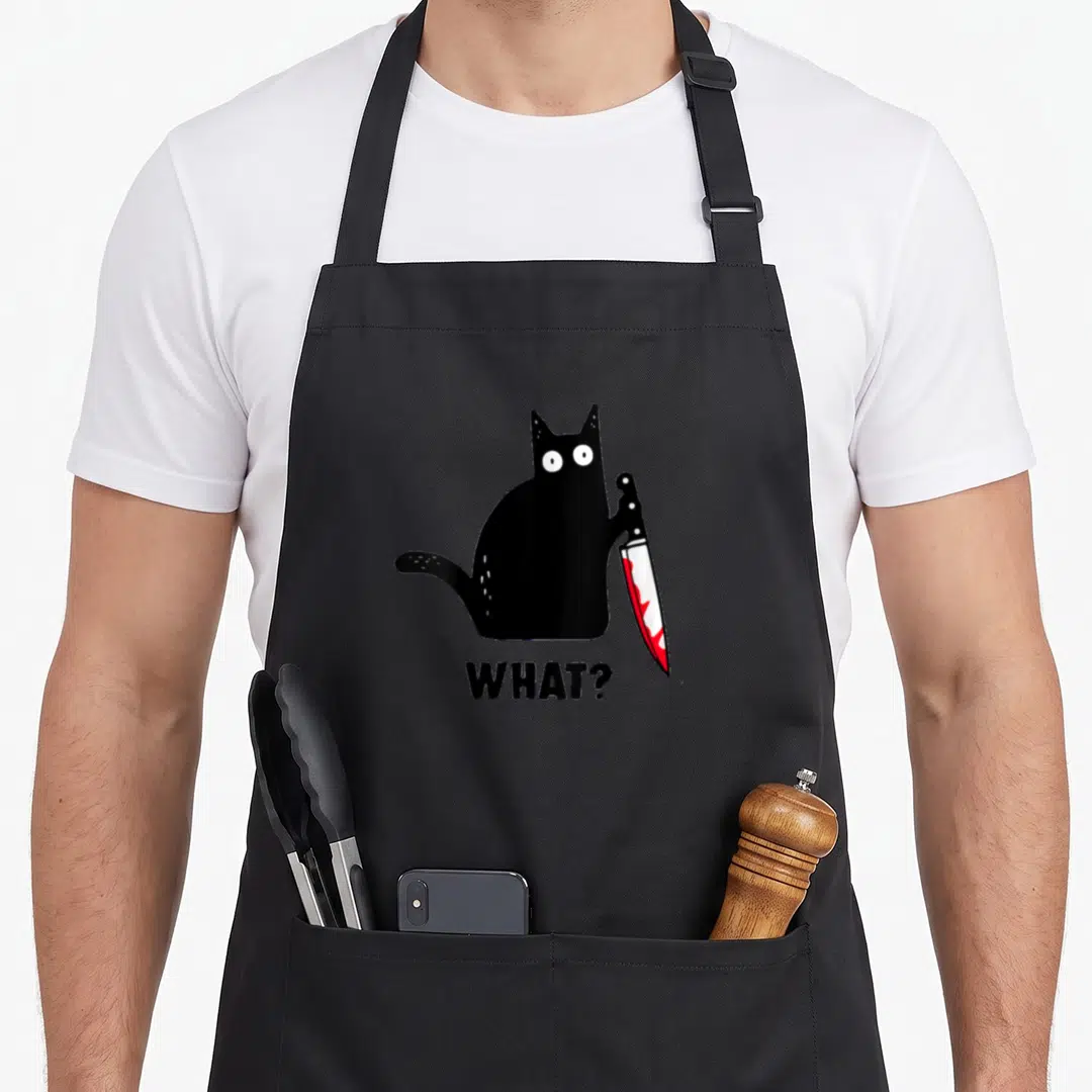 Murderous knife black cat apron - Black cartoon cat holding bloody knife with WHAT? text below — shown on a black cotton canvas apron against a white background