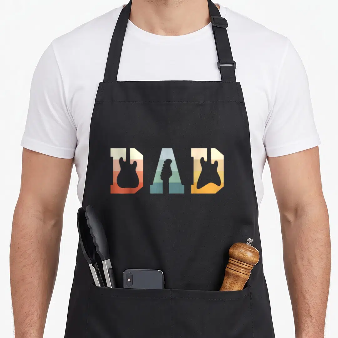 Acoustic music dad apron - Retro striped DAD text with electric guitar body and headstock silhouettes in multicolor — shown on a black cotton canvas apron against a white background