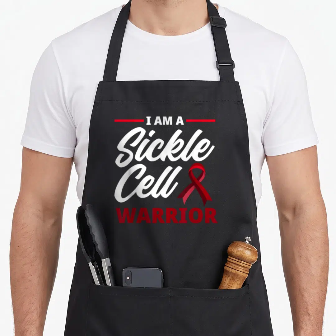 Warrior sickle cell awareness apron - Red and white stacked text reading I AM A Sickle Cell WARRIOR next to a red — shown on a black cotton canvas apron against a white background