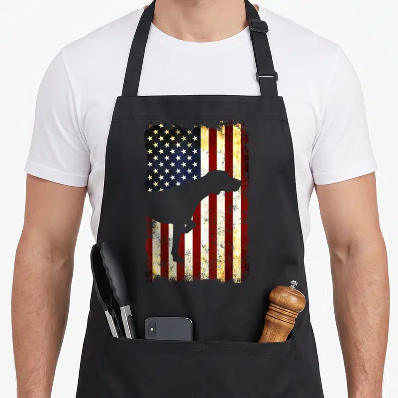 Silhouette pointer apron - Grey dog silhouette standing in front of a weathered red white and blue flag pattern — shown on a black cotton canvas apron against a white background