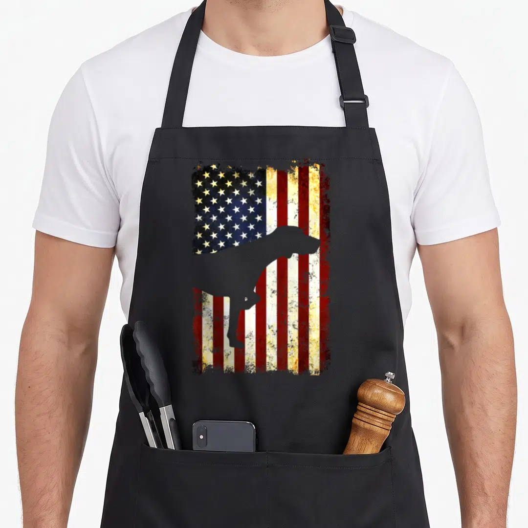 Silhouette pointer apron - Grey dog silhouette standing in front of a weathered red white and blue flag pattern — shown on a black cotton canvas apron against a white background