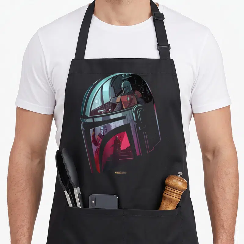 Helmet classical apron - Mandalorian helmet shape framing cockpit and walking scenes in silver, blue, red, and grey — shown on a black cotton canvas apron against a white background