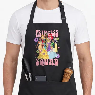 Epic floral apron - PRINCESS SQUAD text surrounding ten princesses with flowers and hearts in pink yellow blue purple — shown on a black cotton canvas apron against a white background