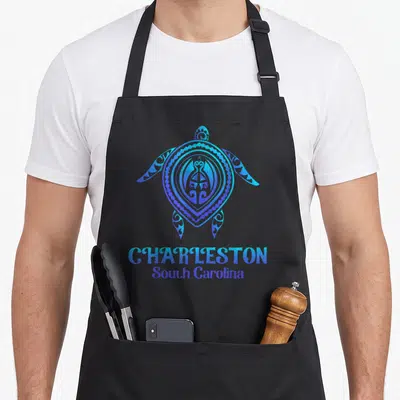 Sea charleston apron - Stylized blue and purple turtle above stacked Charleston South Carolina text — shown on a black cotton canvas apron against a white background
