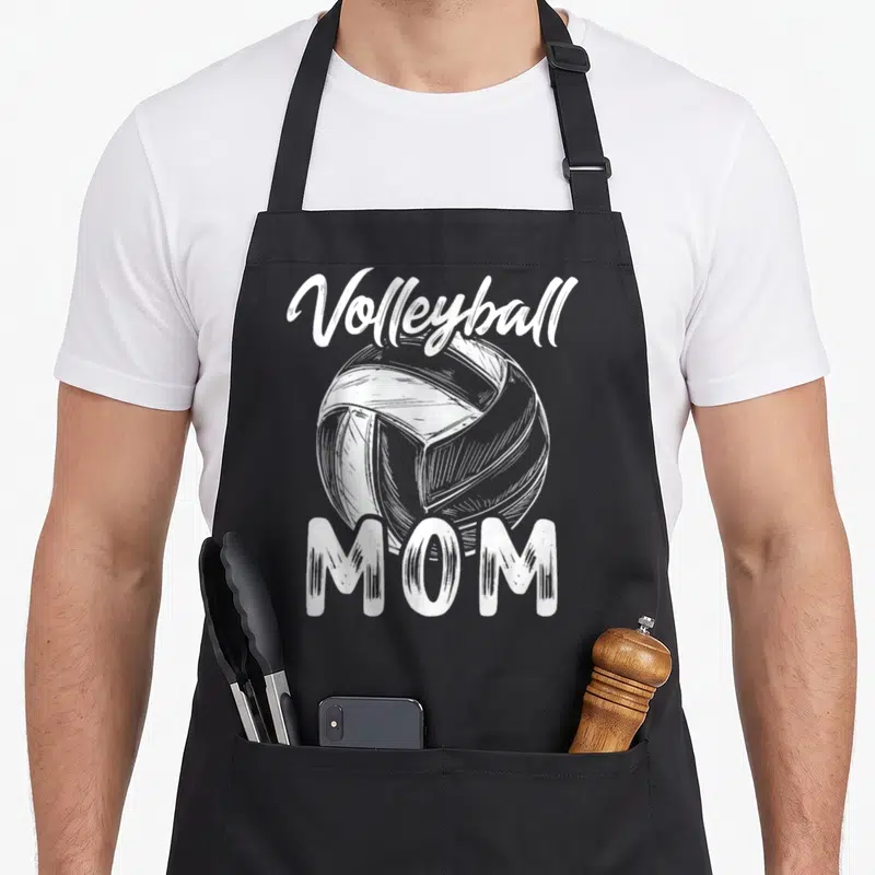 Volleyball family aprons - White sketched volleyball with arched Volleyball text and block MOM letters on black fabric — shown on a black cotton canvas apron against a white background