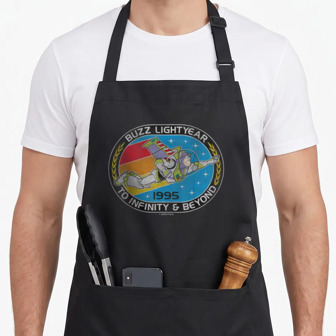 Infinity dog breed aprons - Buzz Lightyear flying in a circular badge with To Infinity and Beyond text and 1995 date — shown on a black cotton canvas apron against a white background
