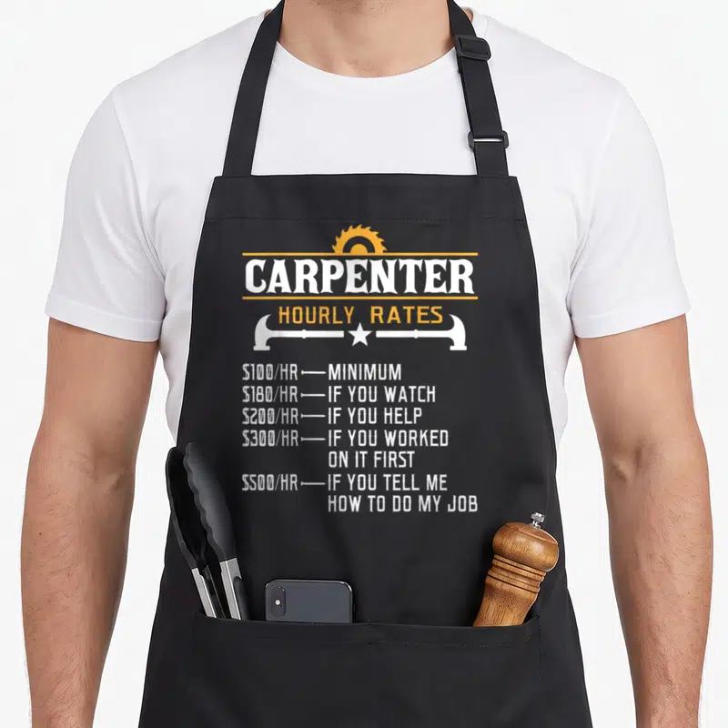 Hourly carpentry apron - Carpenter hourly rates text with saw blade and hammer divider in white and orange — shown on a black cotton canvas apron against a white background