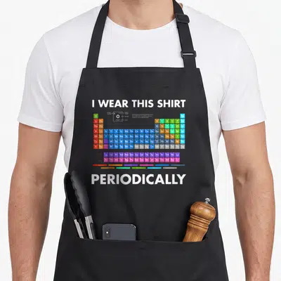 Periodically chemistry apron - I WEAR THIS SHIRT PERIODICALLY text above multicolor periodic table grid — shown on a black cotton canvas apron against a white background