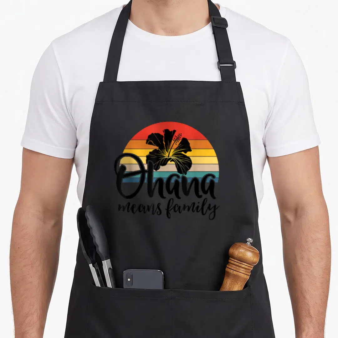 Ohana hawaiian apron - Black hibiscus on red orange yellow teal stripes with Ohana means family script text — shown on a black cotton canvas apron against a white background