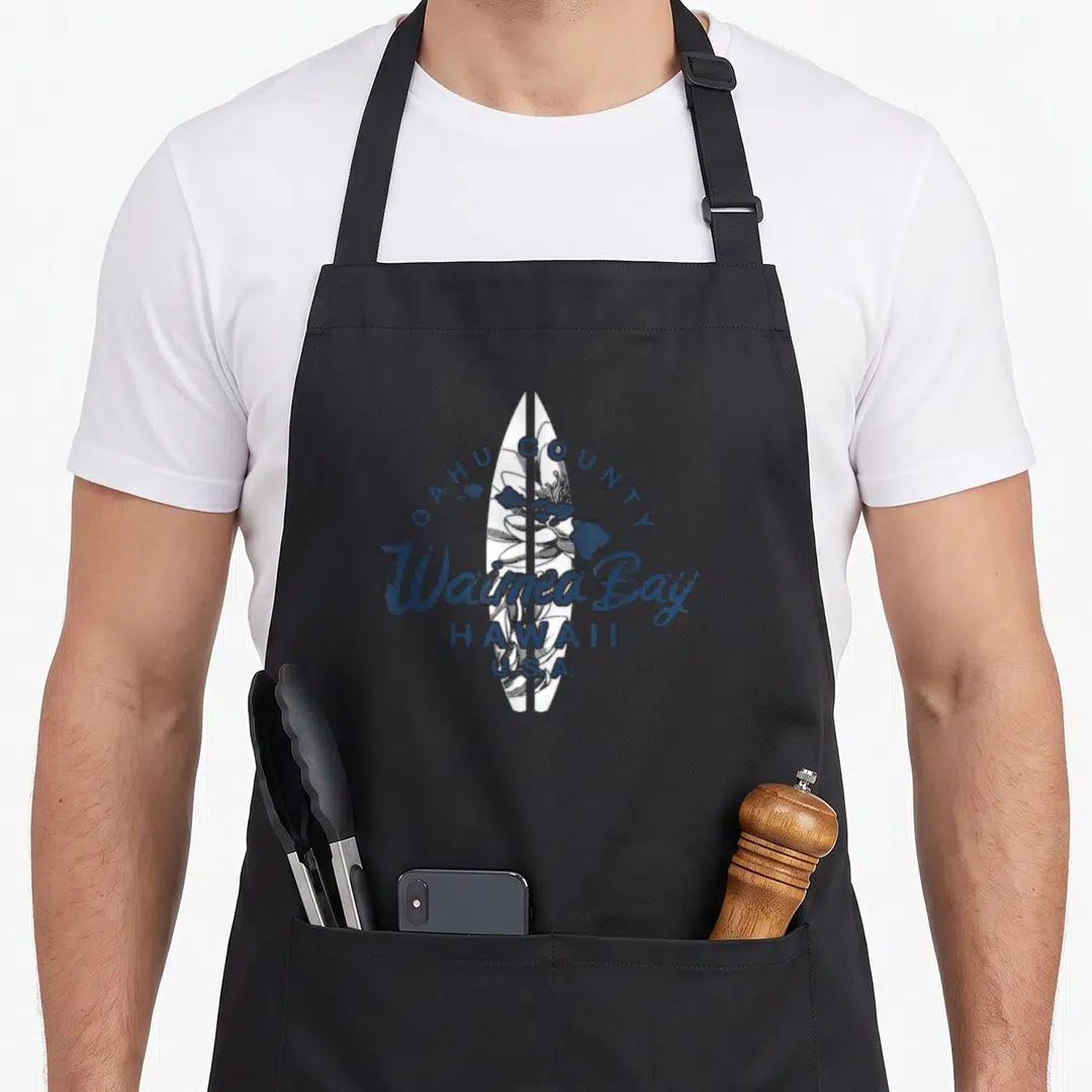 Waimea hawaiian apron - White surfboard with blue flower sketch and Oahu County Waimea Bay text in distressed style — shown on a black cotton canvas apron against a white background
