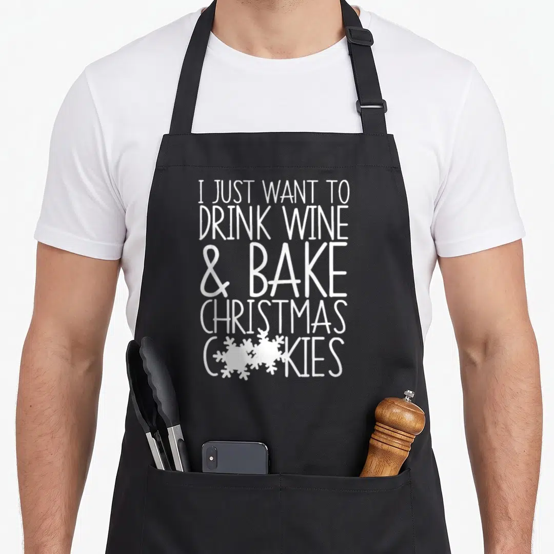Drink women's christmas aprons - White stacked text I Just Want To Drink Wine Bake Christmas Cookies with two — shown on a black cotton canvas apron against a white background