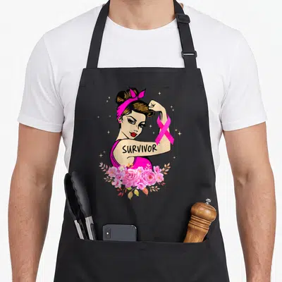 Rosie breast cancer awareness aprons - Cartoon woman flexing arm with SURVIVOR text, pink ribbon, and flowers — shown on a black cotton canvas apron against a white background