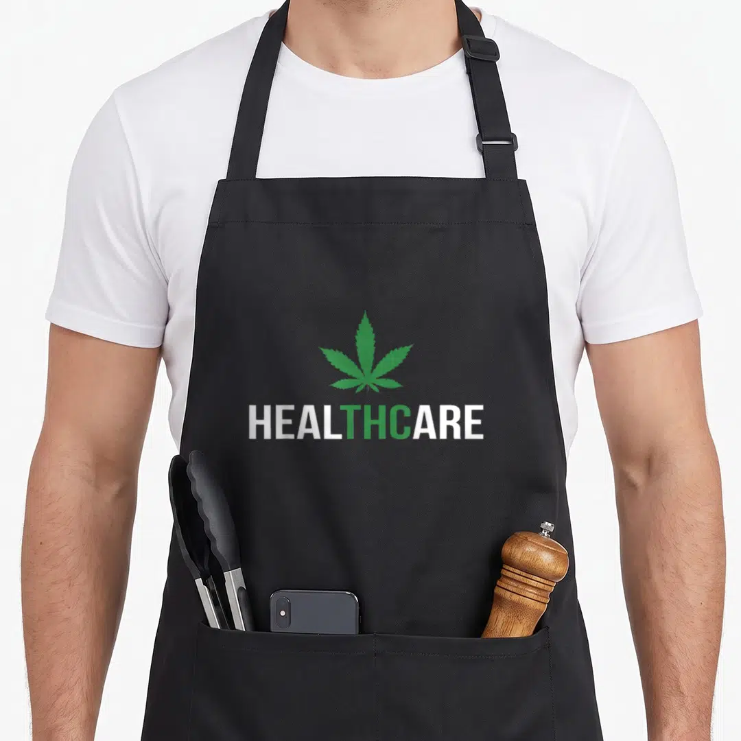 Medical healthcare apron - Green cannabis leaf above white and green HEALTHCARE text — shown on a black cotton canvas apron against a white background