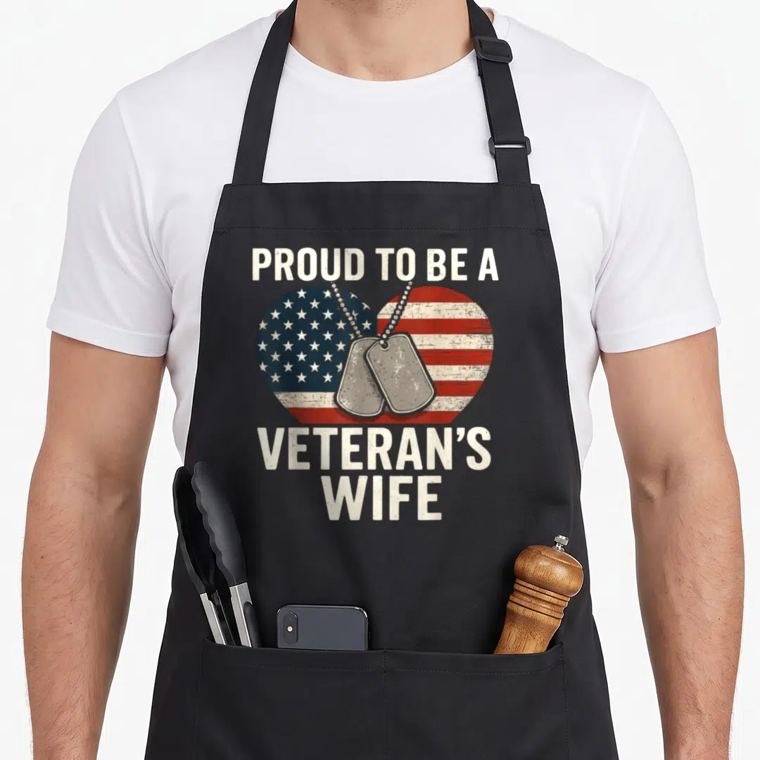 Proud veteran patriotic apron - Distressed heart with US flag and two grey dog tags reading PROUD TO BE A VETERAN'S WIFE — shown on a black cotton canvas apron against a white background