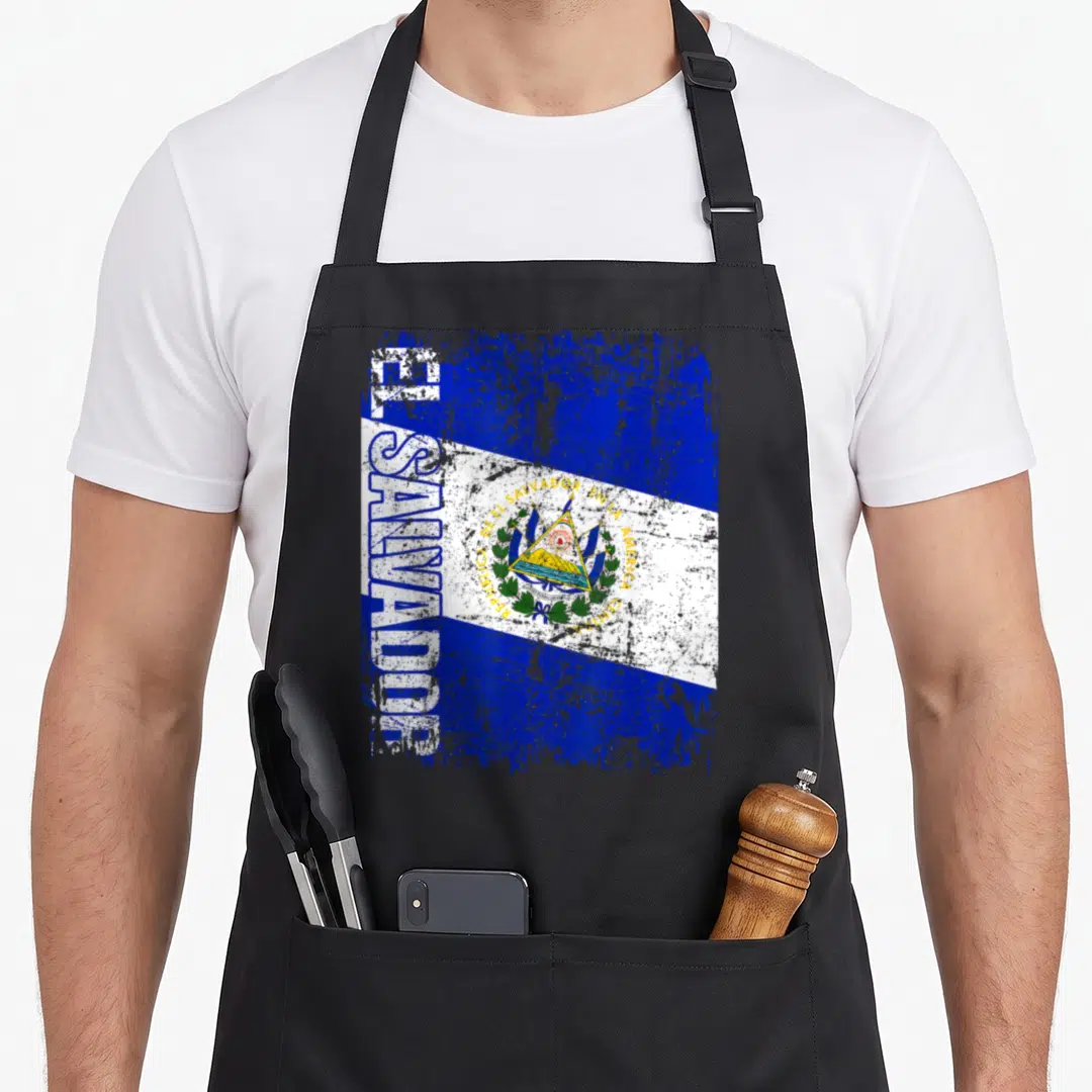 Distressed el cook apron - Vertical EL SALVADOR text beside blue white distressed flag coat of arms — shown on a black cotton canvas apron against a white background