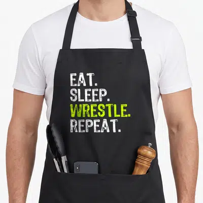 Eat wrestling apron - Stacked Eat Sleep Wrestle Repeat text in white and lime green distressed font — shown on a black cotton canvas apron against a white background