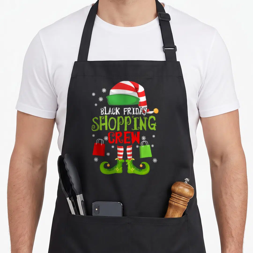 Elf black friday apron - Cartoon elf hat and curled shoes flanking BLACK FRIDAY SHOPPING CREW text with red and green — shown on a black cotton canvas apron against a white background