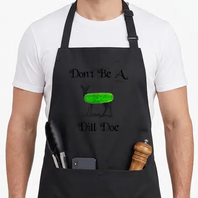 Play pickle apron - Cartoon deer with green pickle across body and Don't Be A Dill Doe text — shown on a black cotton canvas apron against a white background