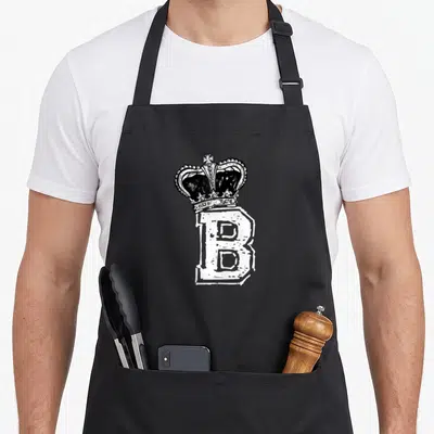 Queen bee apron - Black crown sitting on top of a large white distressed letter B in line art — shown on a black cotton canvas apron against a white background