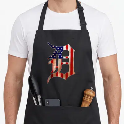 Flag detroit apron - Distressed American flag pattern filling a large stylized Old English letter D — shown on a black cotton canvas apron against a white background