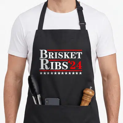 Rib brisket apron - BRISKET RIBS '24 text in white and red with horizontal lines and row of white stars — shown on a black cotton canvas apron against a white background