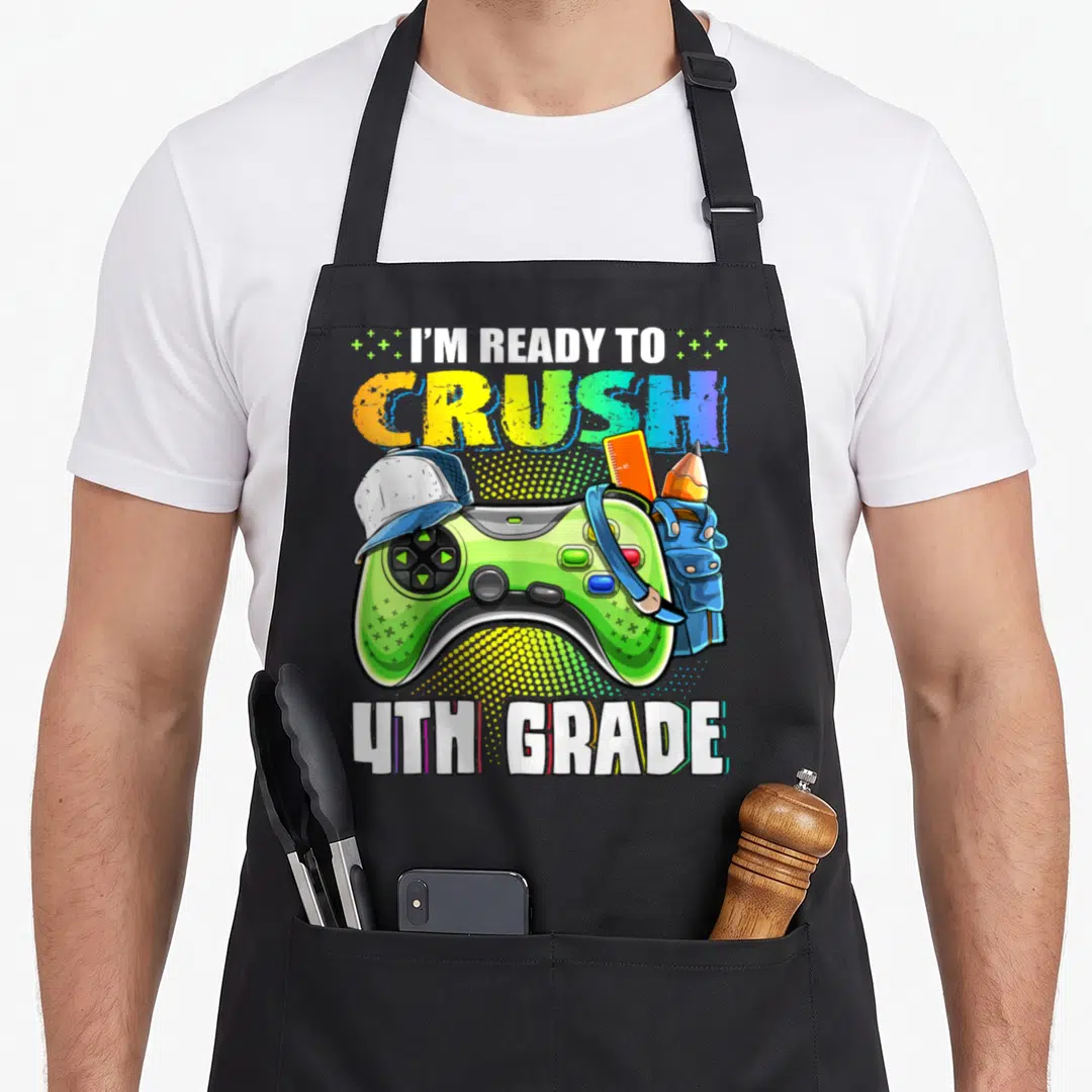 Ready video game apron - Green game controller with cap and school supplies under I'M READY TO CRUSH 4TH GRADE text — shown on a black cotton canvas apron against a white background