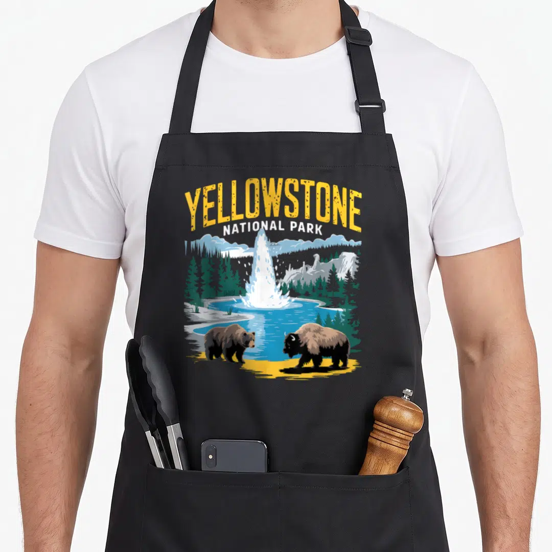 Bison bear apron - Retro Yellowstone National Park print with geyser, bear, and bison in yellow blue green and brown — shown on a black cotton canvas apron against a white background