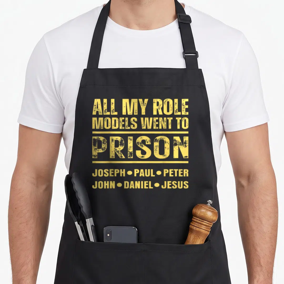 Role model apron - Yellow text listing biblical names Joseph Paul Peter John Daniel Jesus under the word PRISON — shown on a black cotton canvas apron against a white background