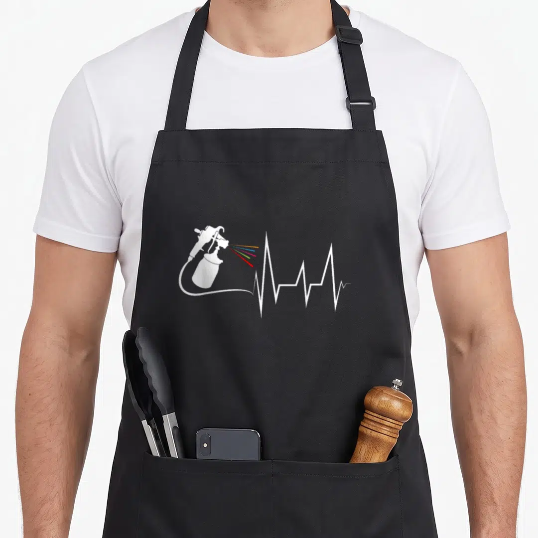 Painter auto apron - White spray gun spraying red orange yellow blue purple lines forming a white EKG heartbeat pulse — shown on a black cotton canvas apron against a white background
