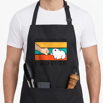 Cute pig guinea dad apron - Cartoon fist bumping a white guinea pig paw over orange teal and grey stripes with text — shown on a black cotton canvas apron against a white background