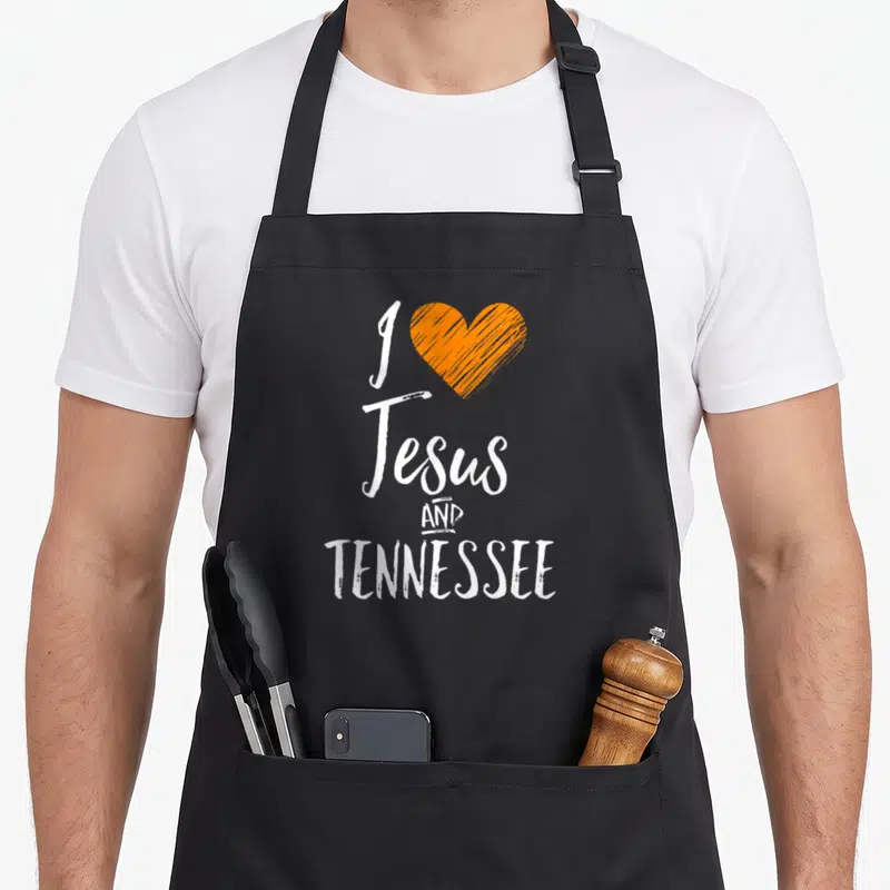 Jesus tennessee men women kids apron - White text I Jesus AND TENNESSEE next to an orange sketched heart — shown on a black cotton canvas apron against a white background