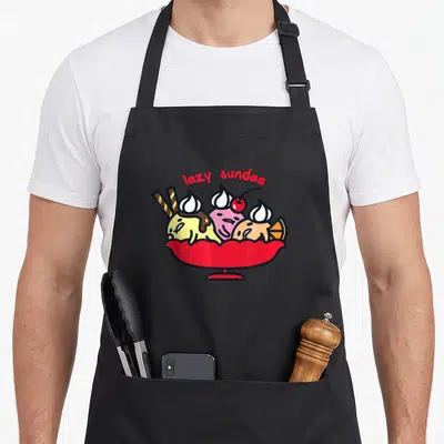 Gudetama ice cream apron - Cartoon lazy sundae bowl with yellow pink and white scoops and red text — shown on a black cotton canvas apron against a white background