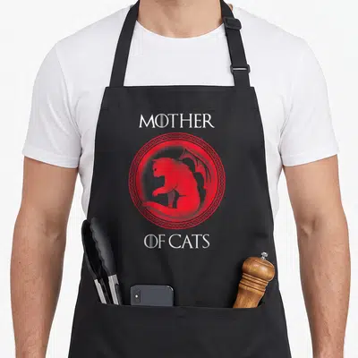 Cat wife mother's day aprons - Red circular emblem with winged cat silhouette and Mother of Cats text — shown on a black cotton canvas apron against a white background