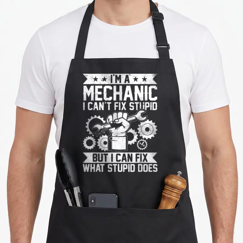 Engineer auto mechanic apron - White distressed hand holding wrench surrounded by gears with stacked banner text — shown on a black cotton canvas apron against a white background