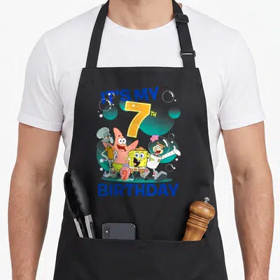 Squarepant 7th birthday apron - Cartoon group of four characters under blue IT'S MY 7TH BIRTHDAY text with bubbles — shown on a black cotton canvas apron against a white background