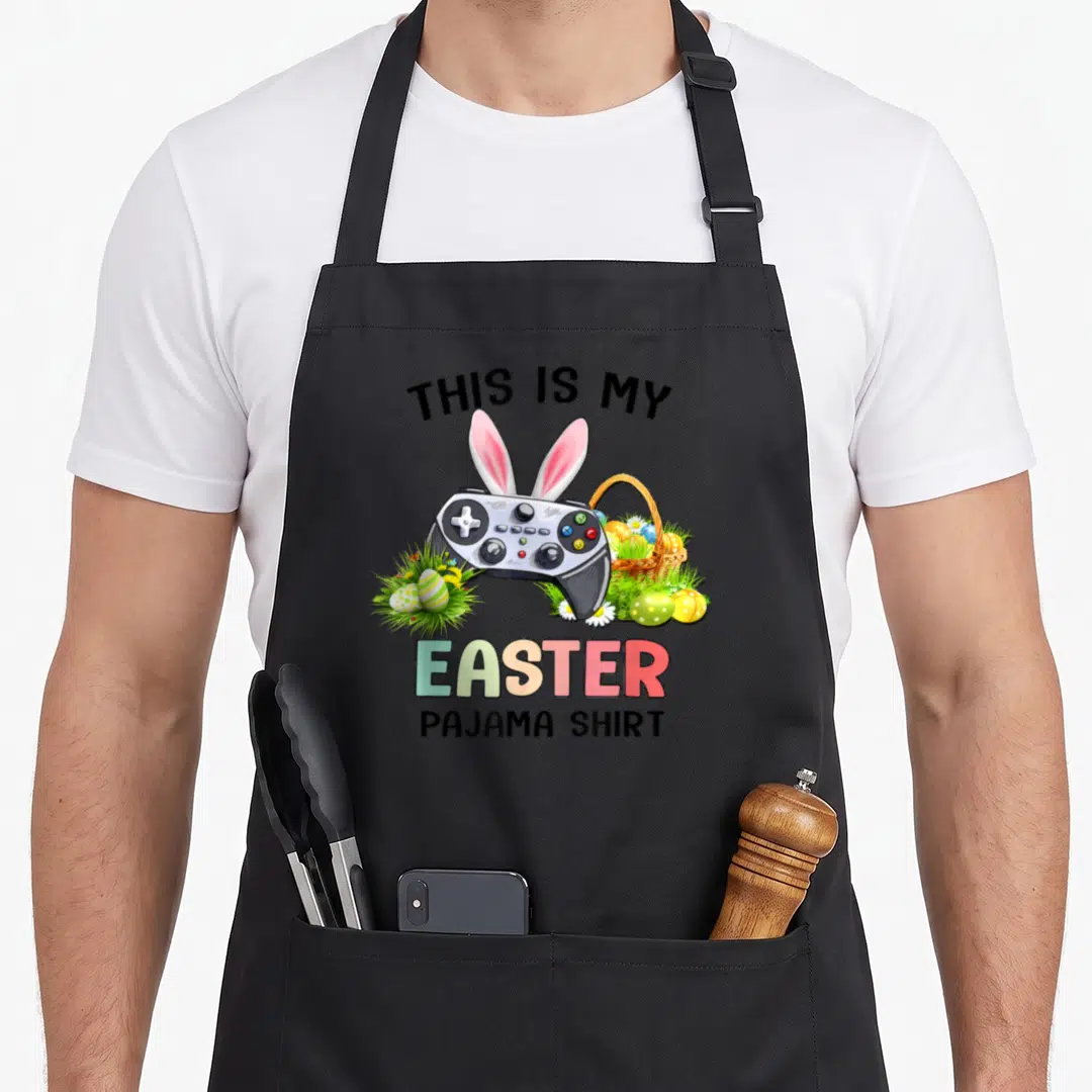 Pajama basket apron - Game controller with pink bunny ears surrounded by Easter eggs, grass, and a basket under printed — shown on a black cotton canvas apron against a white background
