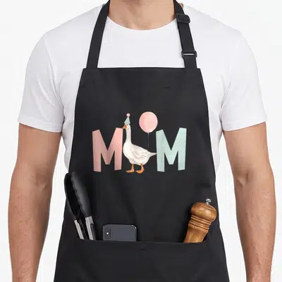 Birthday silly apron - White goose with party hat between pink and blue M letters — shown on a black cotton canvas apron against a white background