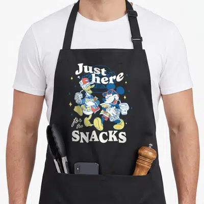 Donald road apron - Mickey and Donald holding snacks with text Just here for the SNACKS in retro colors — shown on a black cotton canvas apron against a white background