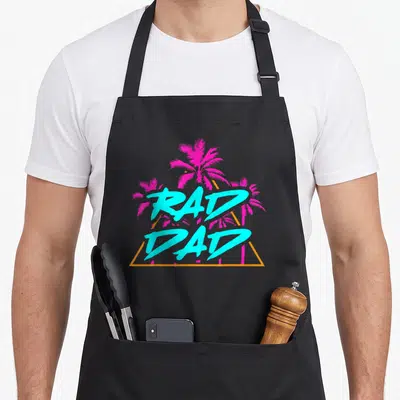 Rad grill daddy apron - Stacked cyan RAD DAD text over three magenta palm trees inside an orange triangle frame — shown on a black cotton canvas apron against a white background