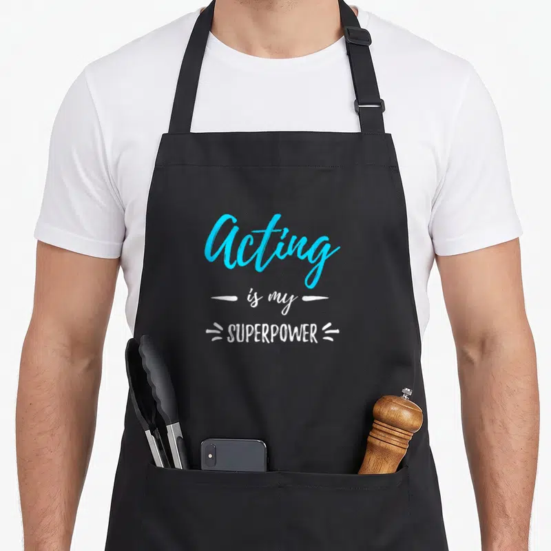 Acting apron or apron - Acting is my SUPERPOWER text in blue and white with decorative dashes — shown on a black cotton canvas apron against a white background