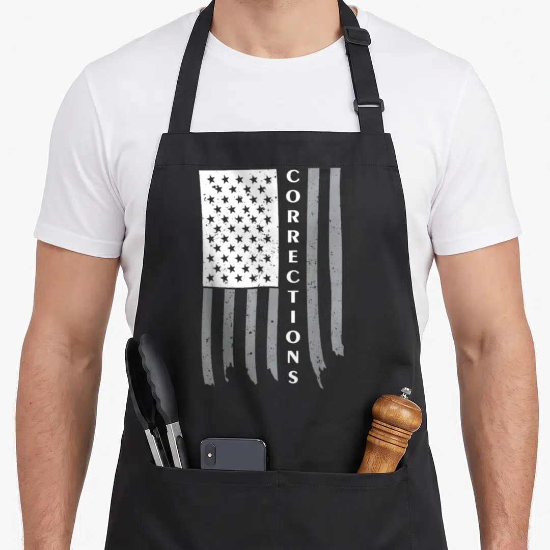 Flag corrections problems apron - Distressed white flag with vertical CORRECTIONS text on black background — shown on a black cotton canvas apron against a white background