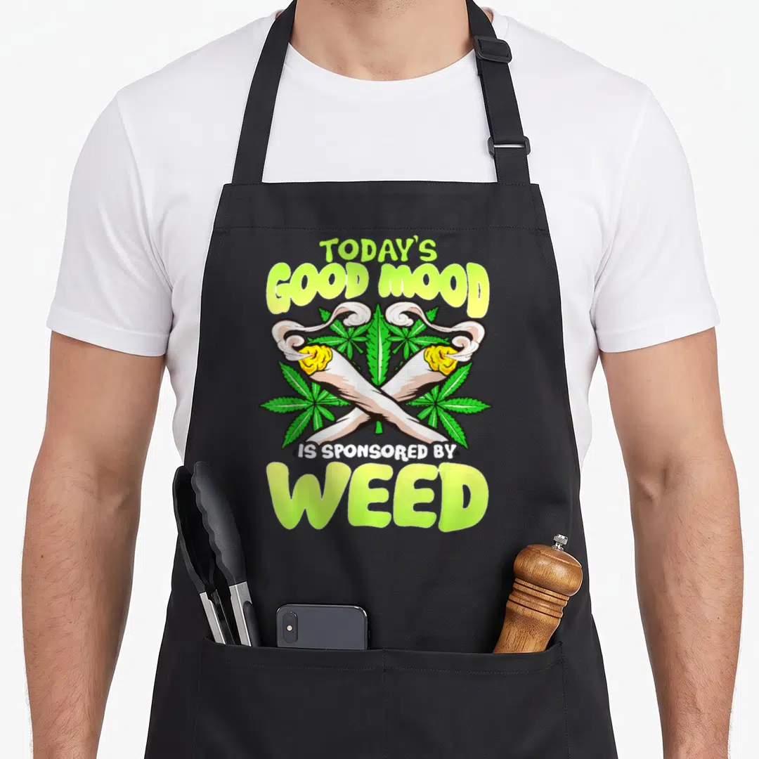 Mood today apron - Crossed joints with green leaves and text Today's Good Mood Is Sponsored By Weed — shown on a black cotton canvas apron against a white background