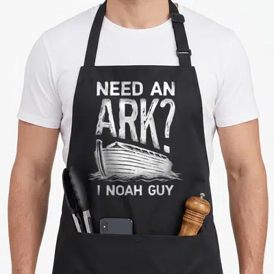 Ark christian apron - Distressed white text Need an Ark I Noah Guy above and below a boat on water — shown on a black cotton canvas apron against a white background
