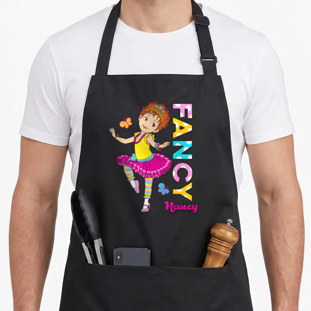 Nancy fancy apron - Dancing cartoon girl next to vertical FANCY text in pink yellow blue and orange polka dots — shown on a black cotton canvas apron against a white background