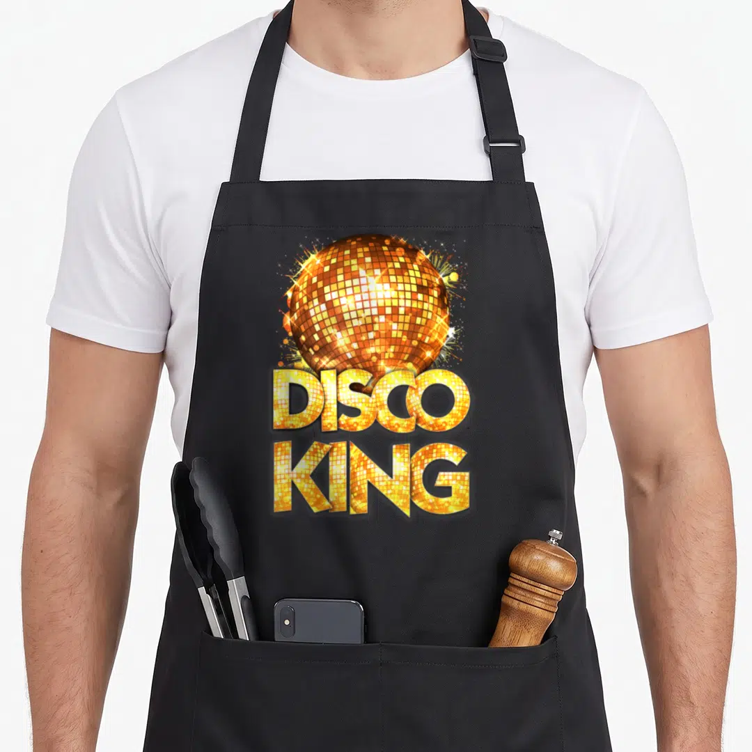 Seventy king apron - Disco ball graphic with stacked DISCO KING text in gold and orange mosaic tiles — shown on a black cotton canvas apron against a white background