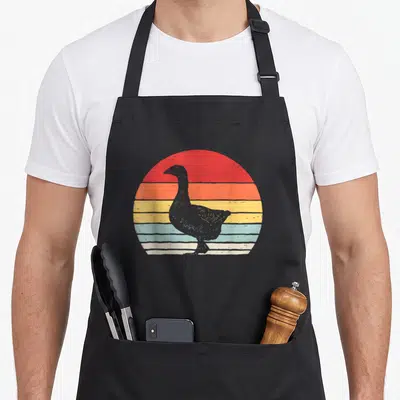 Catch goose apron - Grey goose silhouette centered over horizontal stripes of red, orange, yellow, and blue in a retro — shown on a black cotton canvas apron against a white background